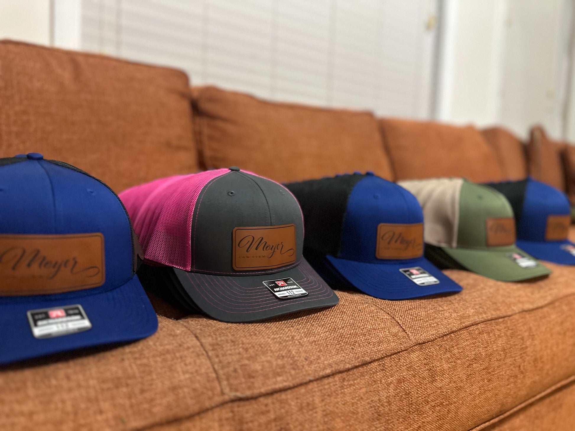 Collection of baseball caps with leather patches on a brown couch