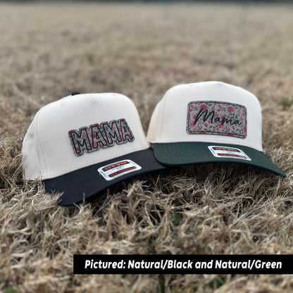 Two trucker hats with 'MAMA' text on them, one in natural color, one with black and natural colors, placed on a grassy surface.