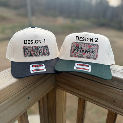 Two trucker hats with 'MAMA' text on them, one in natural color, one with black and natural colors, placed on a porch rail